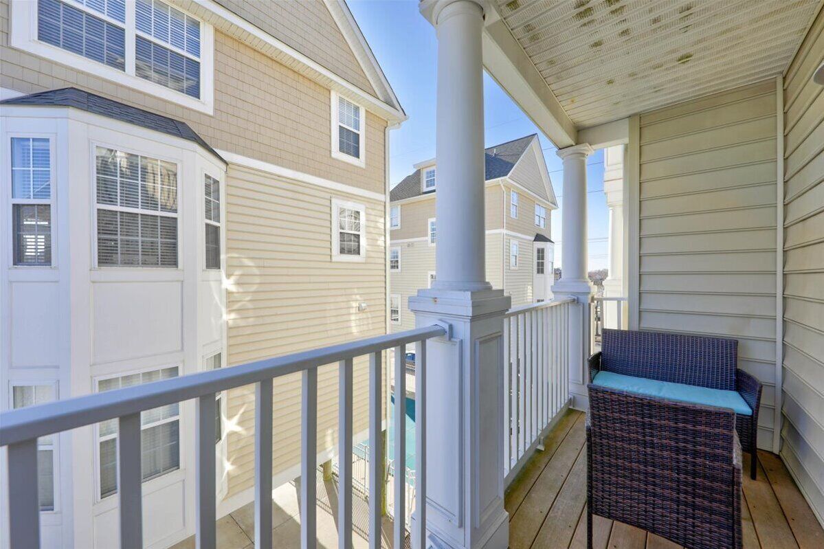 A covered porch with a wicker chair and a white railing.