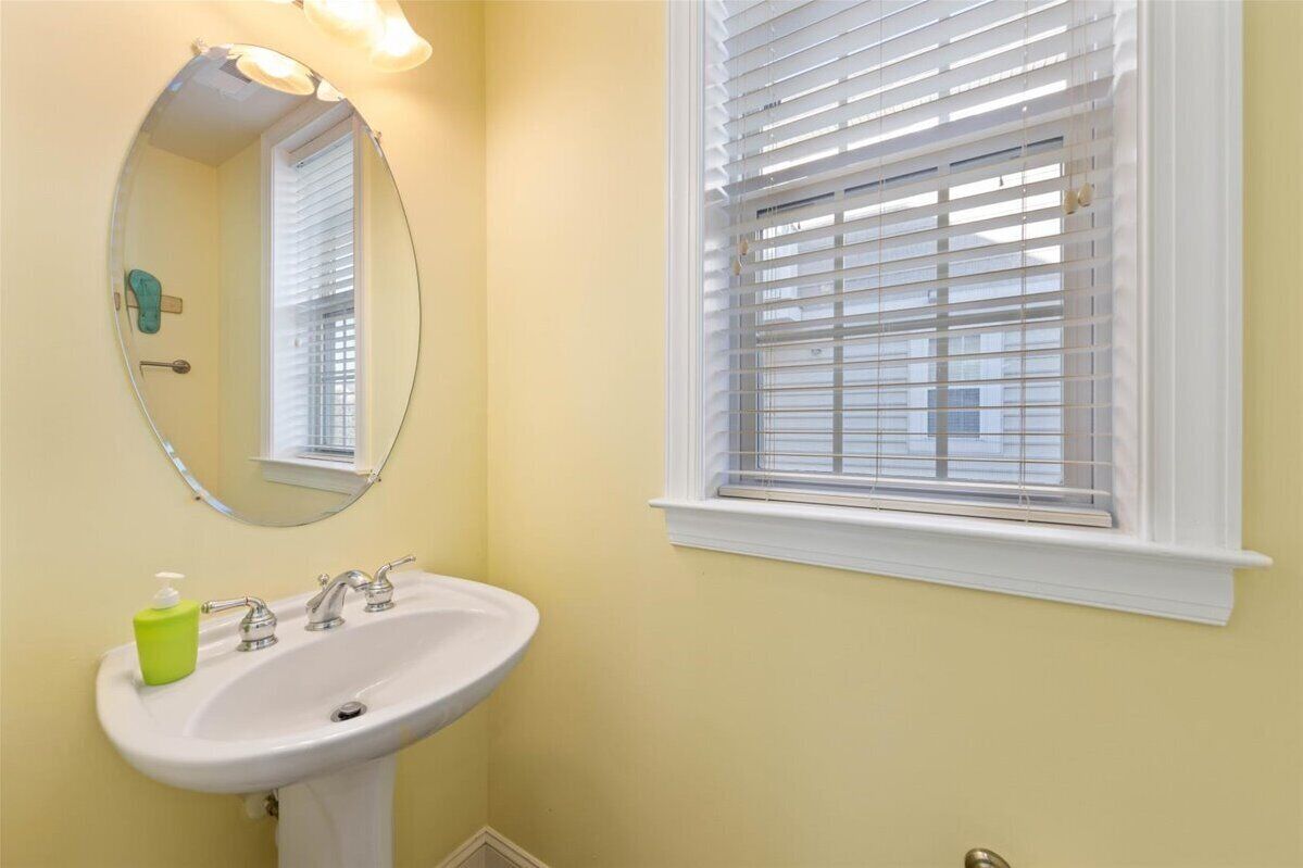 Une salle de bain avec un lavabo blanc, un miroir et une fenêtre avec des stores.