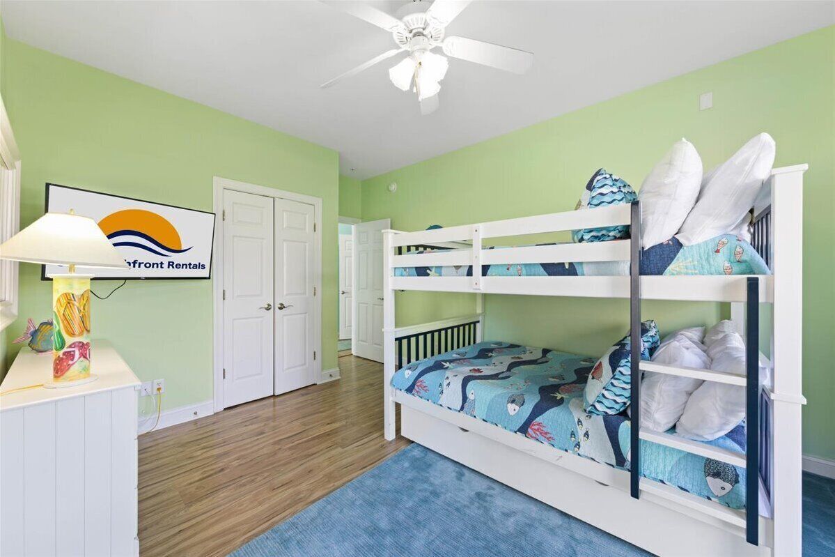 A child's bunk bed room with a ceiling fan, a desk with a lamp, and a sign for 'Front Rentals'.