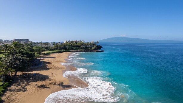 Una playa con agua azul cristalina, una orilla arenosa y un edificio pequeño a la izquierda.