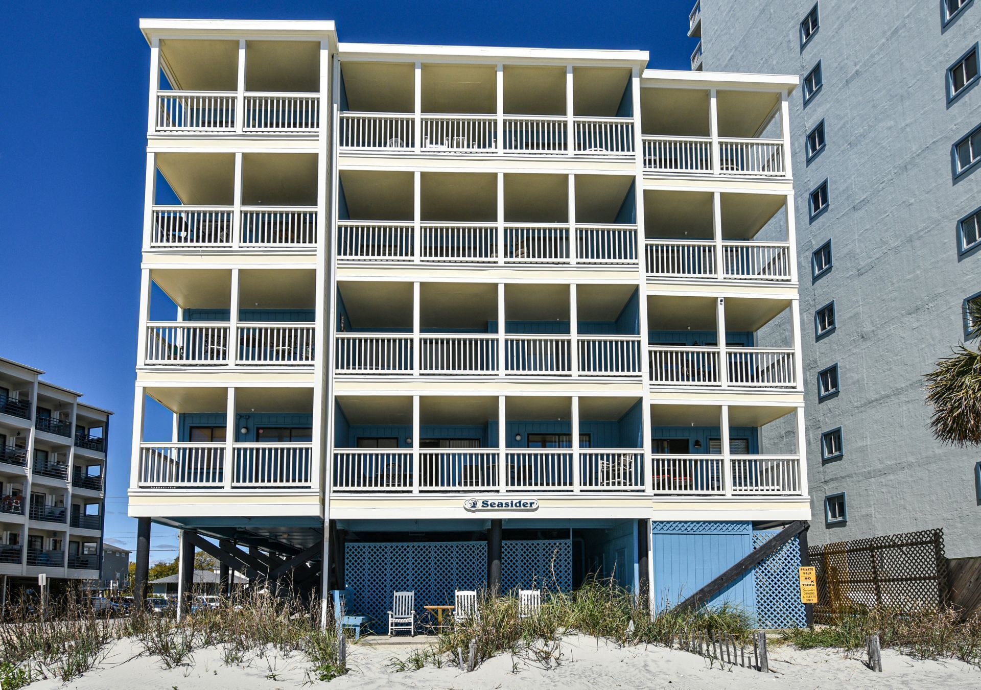 A multi-story hotel with balconies, a beach view, and a sign indicating it is a private walk-thru.