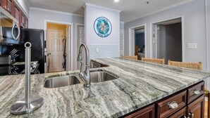 A kitchen with a granite countertop, stainless steel sink, and a welcome sign on the wall. - Seasider 304 - Three Bedrooms, Three Bath Condo in Oceanfront Complex (Garden City Beach)