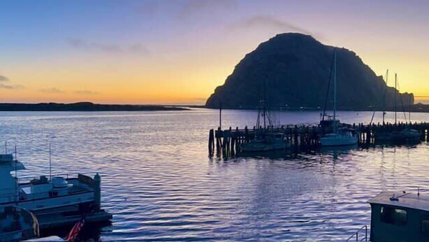 A harbor with boats docked, calm water, and a large island in the background.