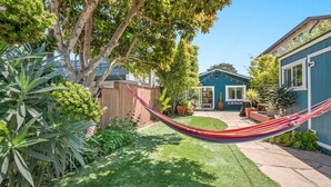 A backyard with a hammock, a wooden fence, and a house with a blue exterior.