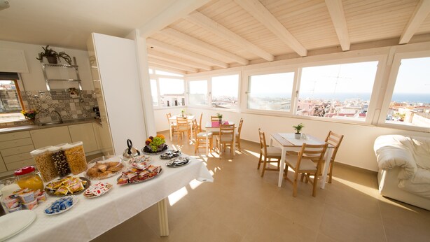A breakfast setup with a table, chairs, and a view of the city through large windows. - La Balestra B&B (Balestrate)