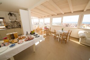 A breakfast setup with a table, chairs, and a view of the city through large windows. - La Balestra B&B (Balestrate)