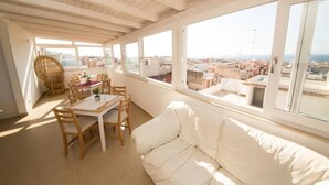 A bright room with a wooden ceiling, a white sofa, a dining table with chairs, and large windows offering a view of buildings and the sea. - La Balestra B&B (Balestrate)