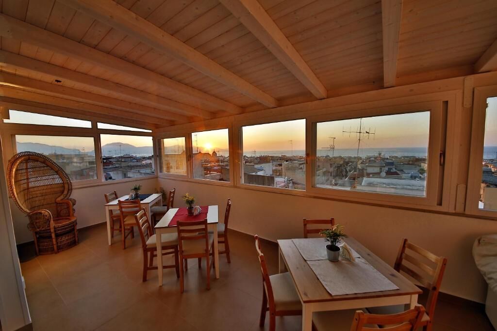 A wooden-floored dining area with large windows overlooking a cityscape at sunset.
