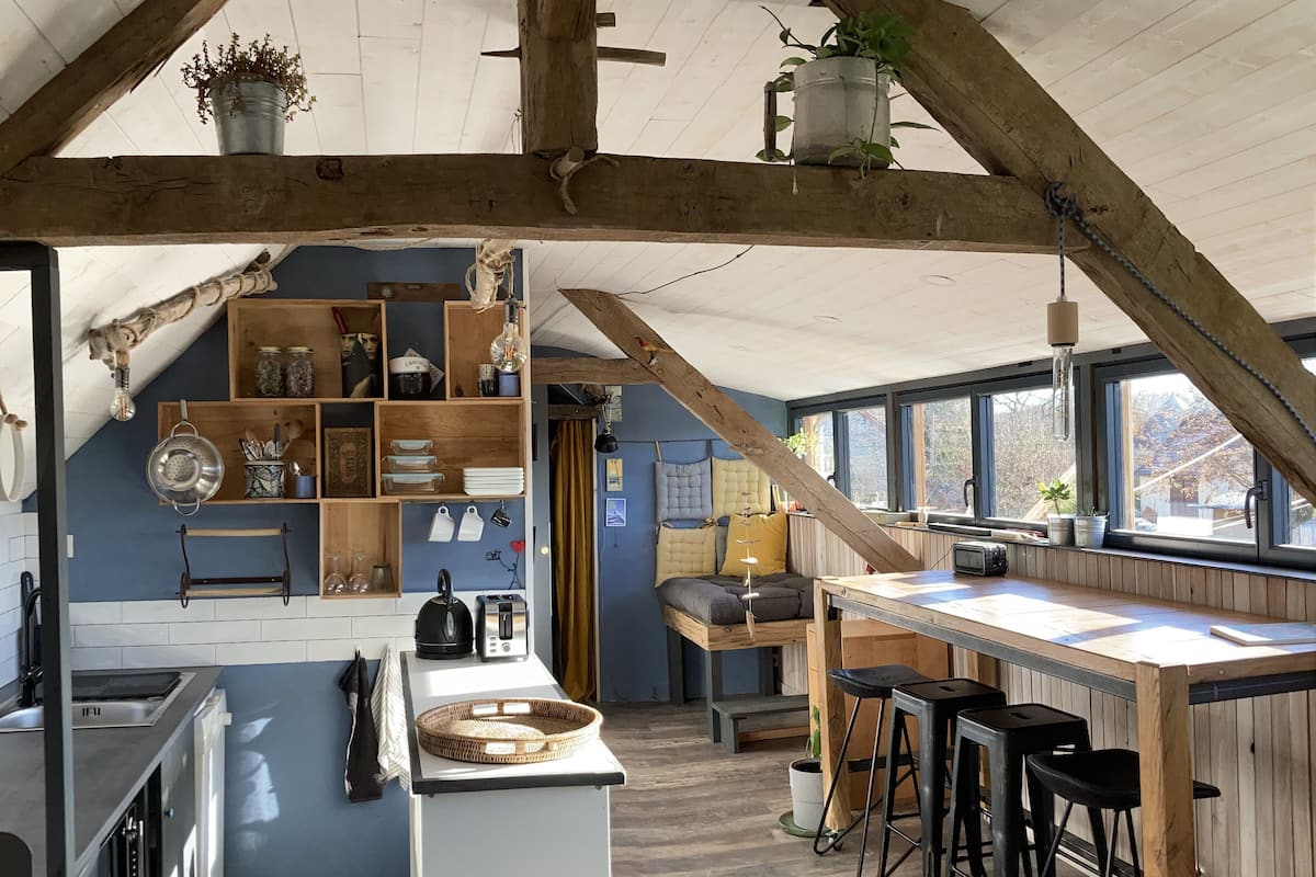 A rustic kitchen with a wooden ceiling, a central island with stools, and a view of the outdoors through large windows.