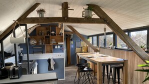 Una cocina rústica con vigas de madera, un comedor con taburetes y vistas al exterior a través de amplias ventanas.