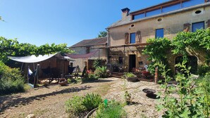 Un edificio de piedra rústico con un patio jardín, mobiliario exterior y plantas trepadoras.