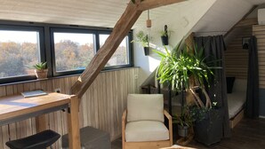 Un dormitorio estilo loft acogedor, con techo inclinado, vigas de madera, un escritorio, una silla y varias plantas en macetas.