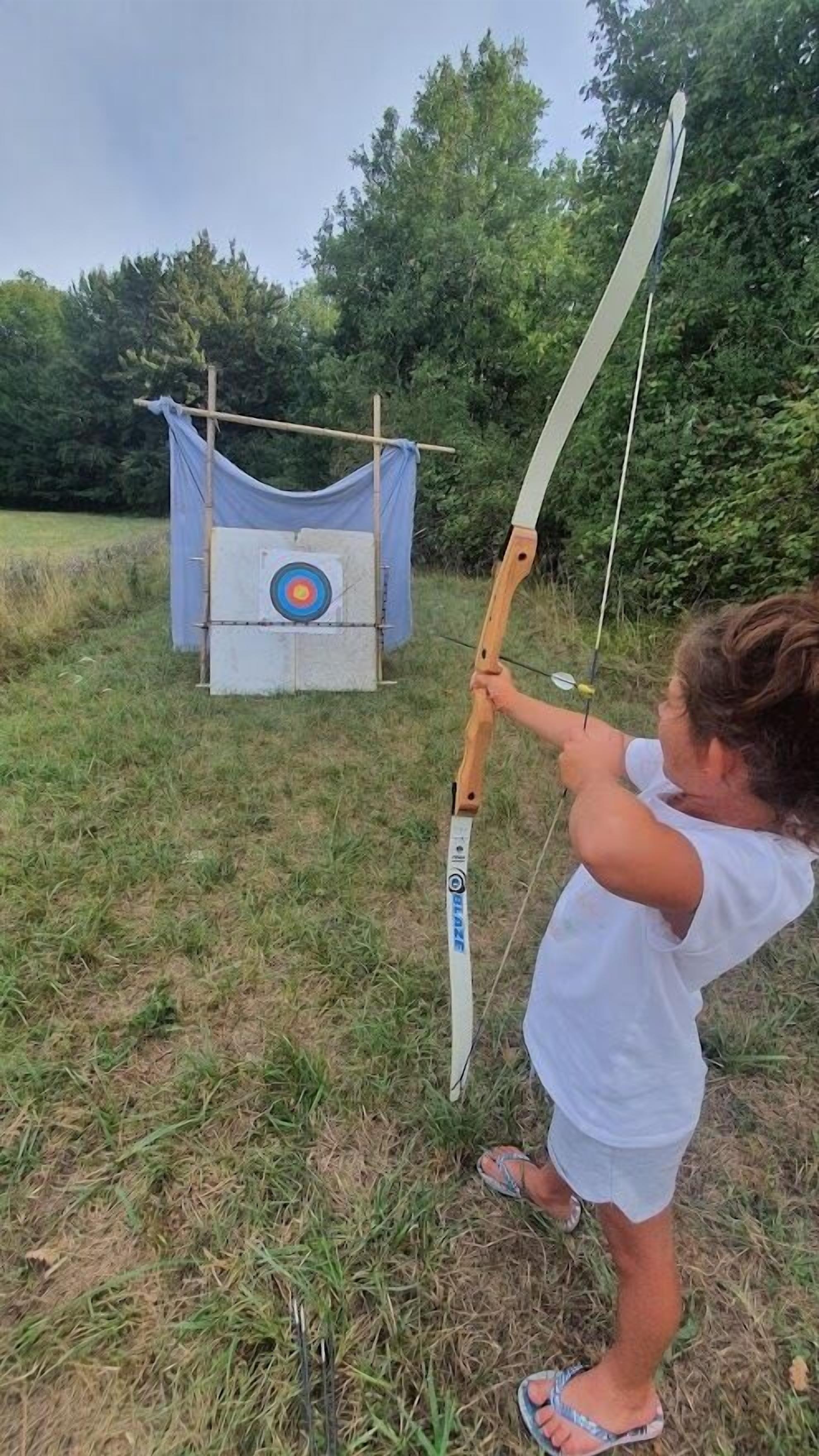A person aiming a bow at an archery target in an outdoor setting.