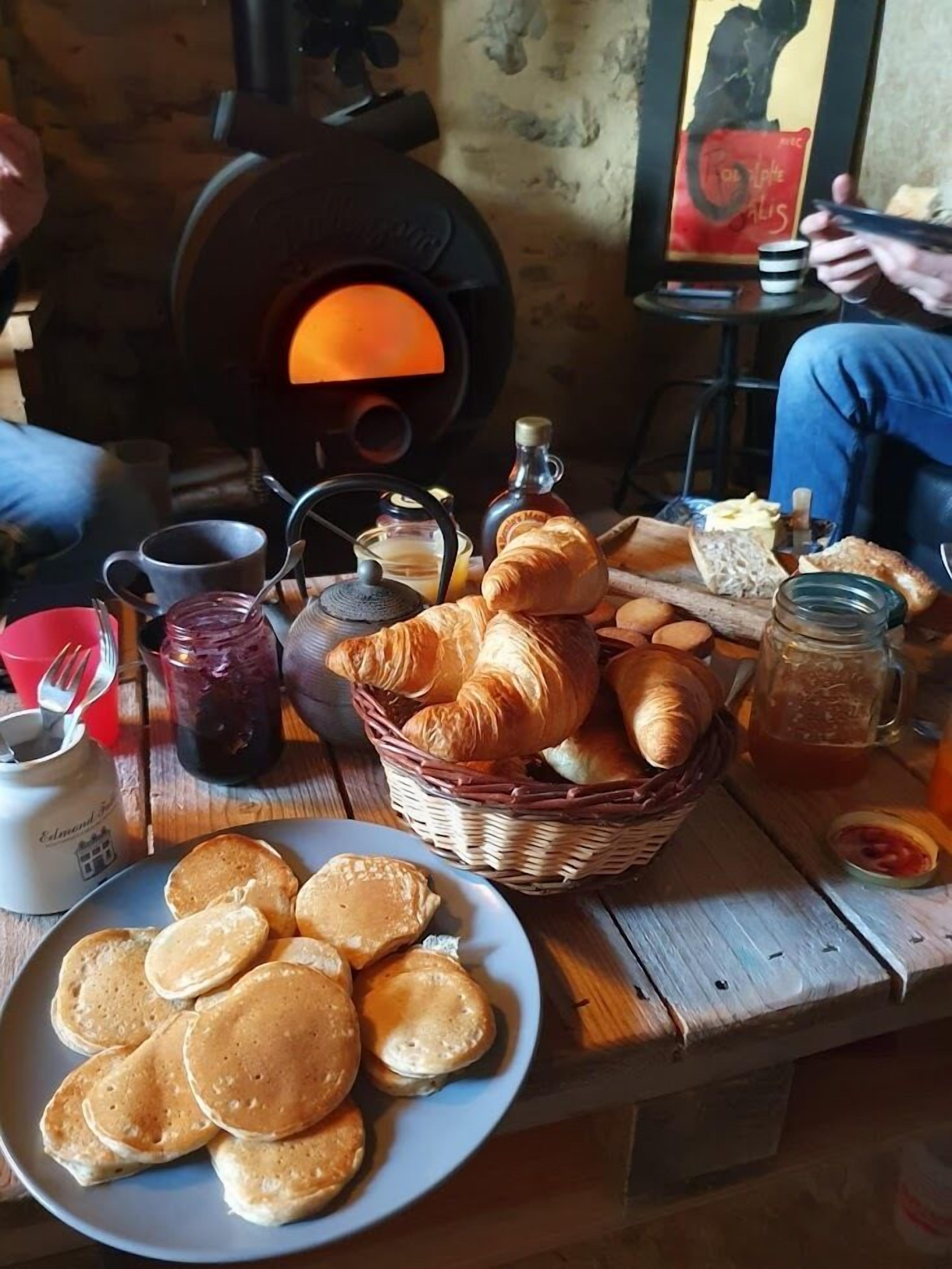 Un ambient de petit esmorzar rústic amb un forn de llenya, pastissos i crepes sobre una taula de fusta.