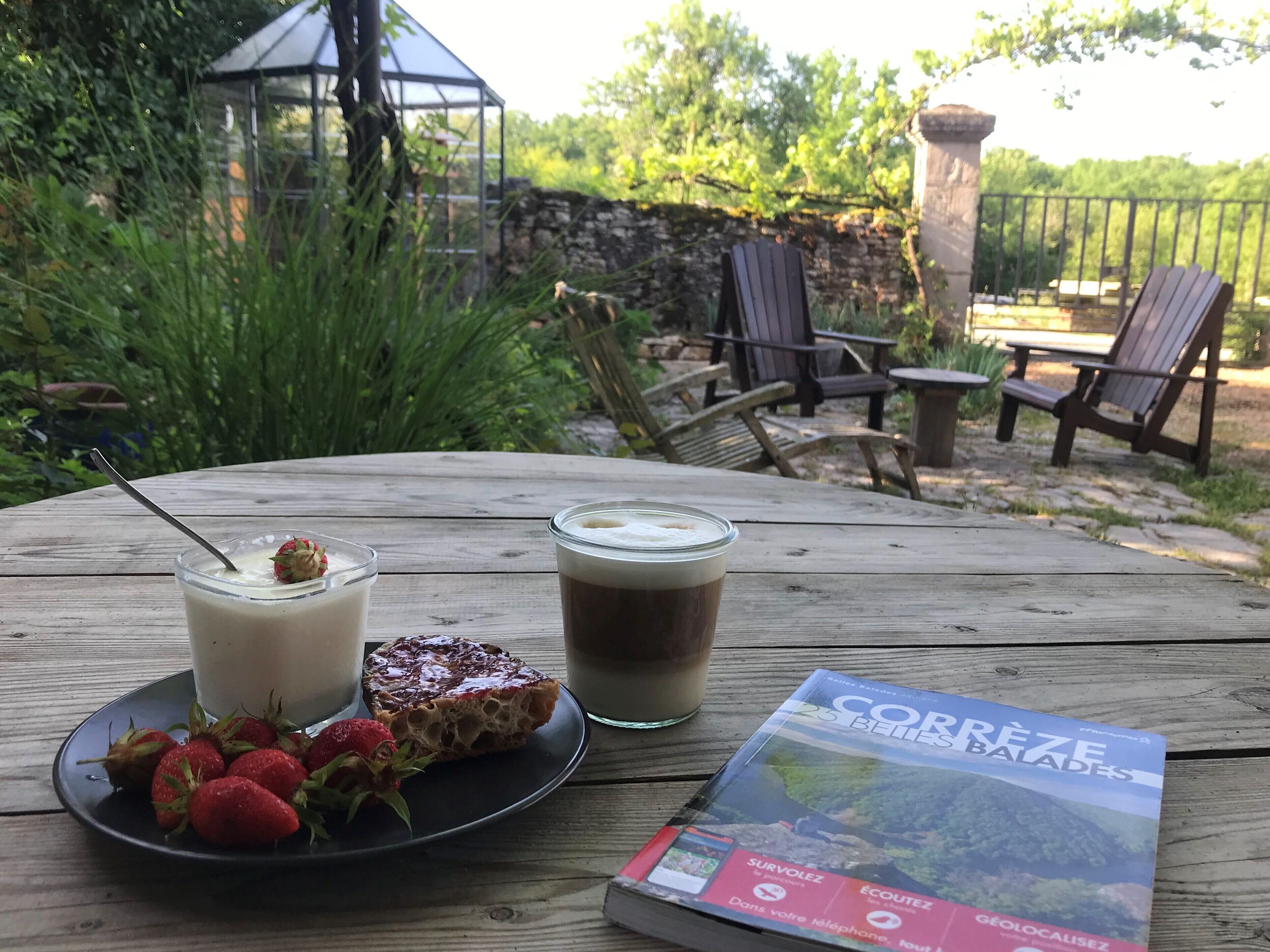 Een houten tafel met een glas melk, een plakje brood met aardbei, een glas koffie en een reisgids.