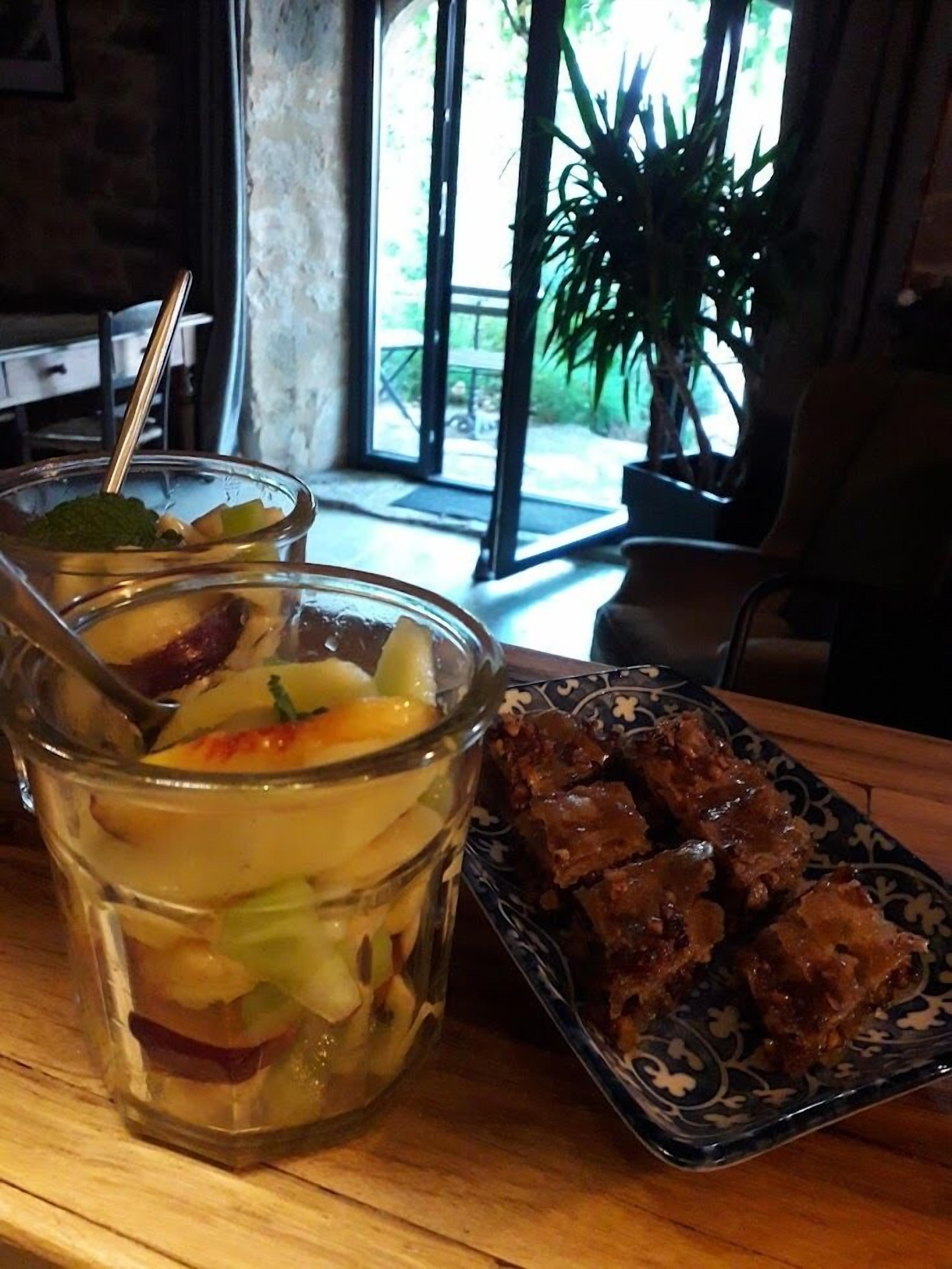 Una mesa con ensalada de frutas en un vaso y un plato de albóndigas.
