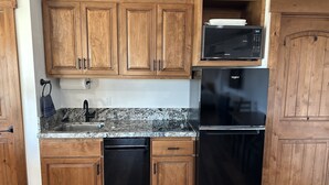 A kitchen with wooden cabinets, a granite countertop, a black dishwasher, a black refrigerator, and a microwave.
