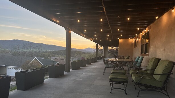 A covered outdoor seating area with a table and chairs, overlooking a scenic landscape.