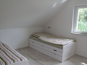 A small, single-bed room with a sloped ceiling and a window providing natural light.