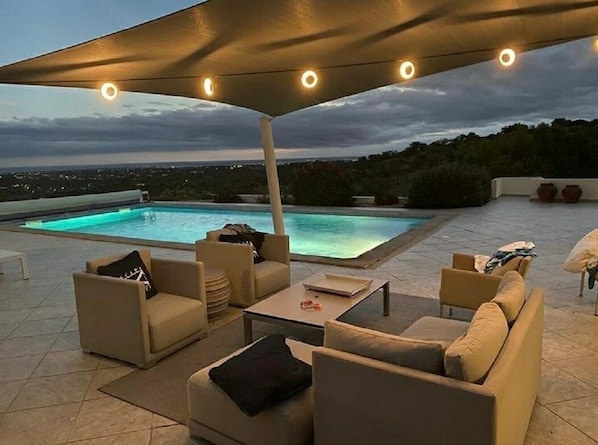 Relax by the pool in a serene outdoor lounge area with a covered seating space and expansive patio views.