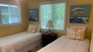 A bedroom with two single beds, a nightstand, and a window with blinds. - Whittier Cottage (Douglas)