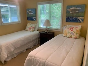 Une chambre avec deux lits simples, une table de chevet et une fenêtre avec des stores.