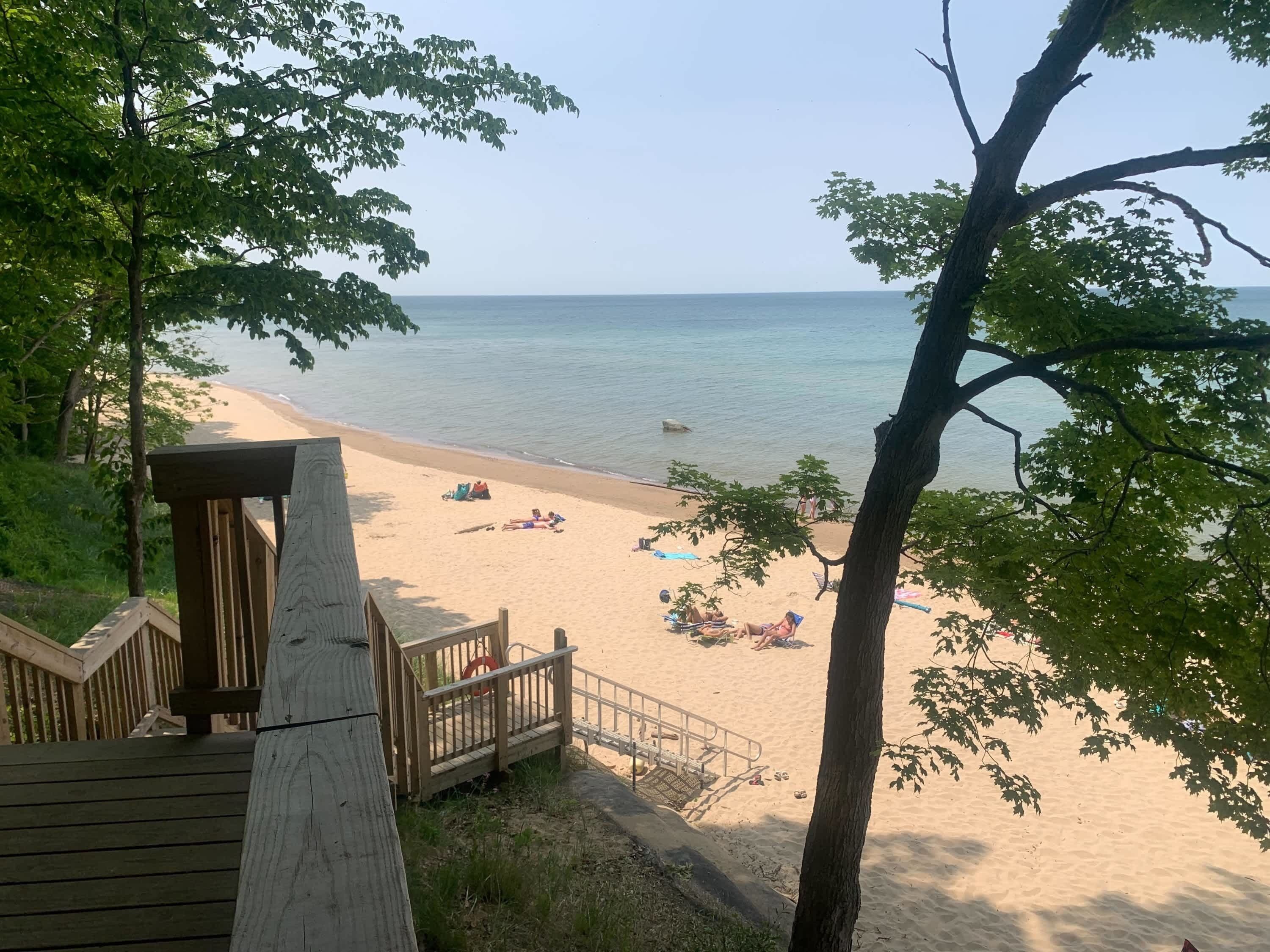 A beach with a wooden deck and a railing, overlooking a sandy shore with people relaxing.