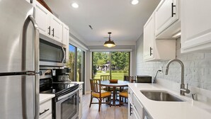 A modern kitchen with stainless steel appliances, a dining area with wooden chairs, and a view of a garden through large windows.