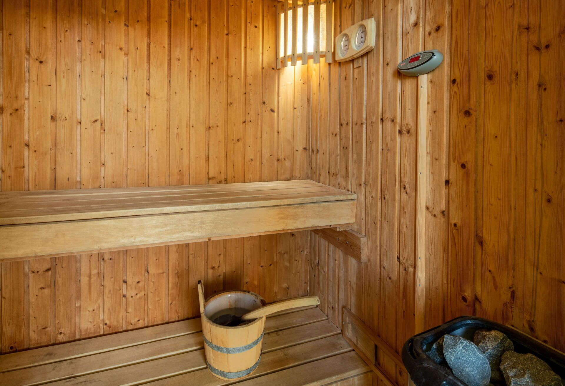 A wooden sauna with a bench, a bucket, and a stone-filled container.