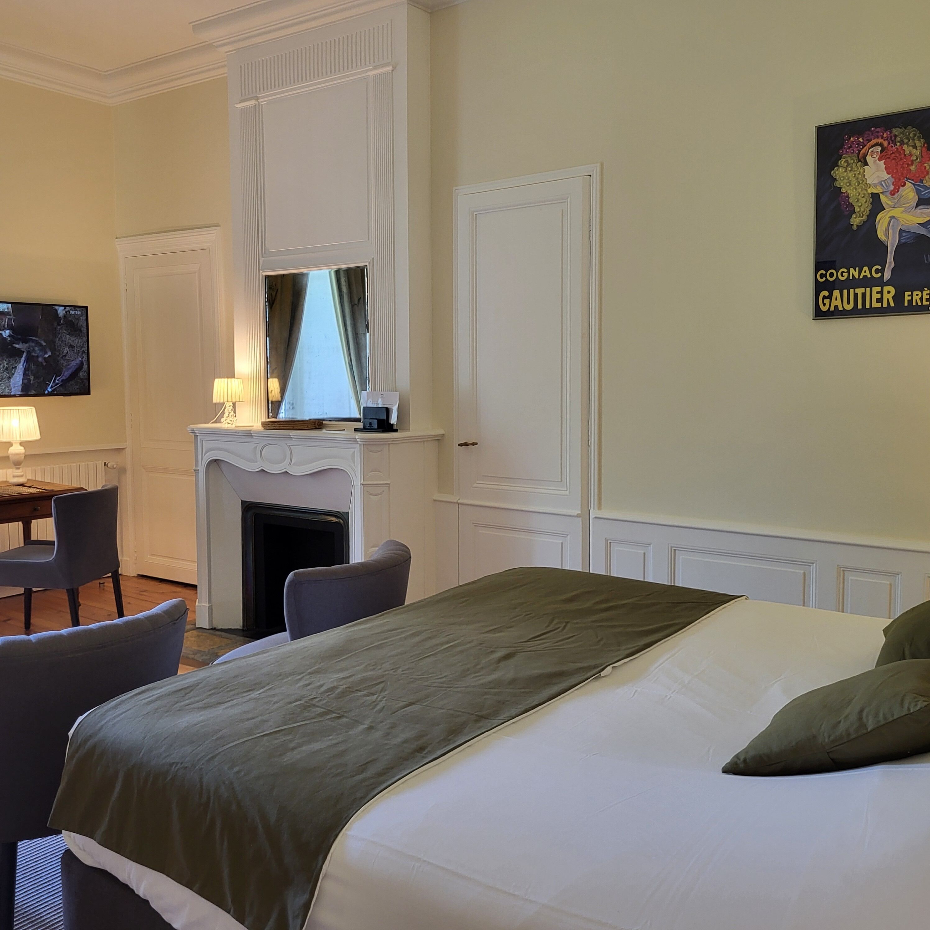 A hotel room with a bed, a desk with a chair, a fireplace, and a television.