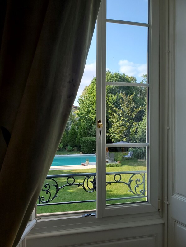Finestra amb vista a una piscina, un jardí amb gespa i una zona de terrassa.