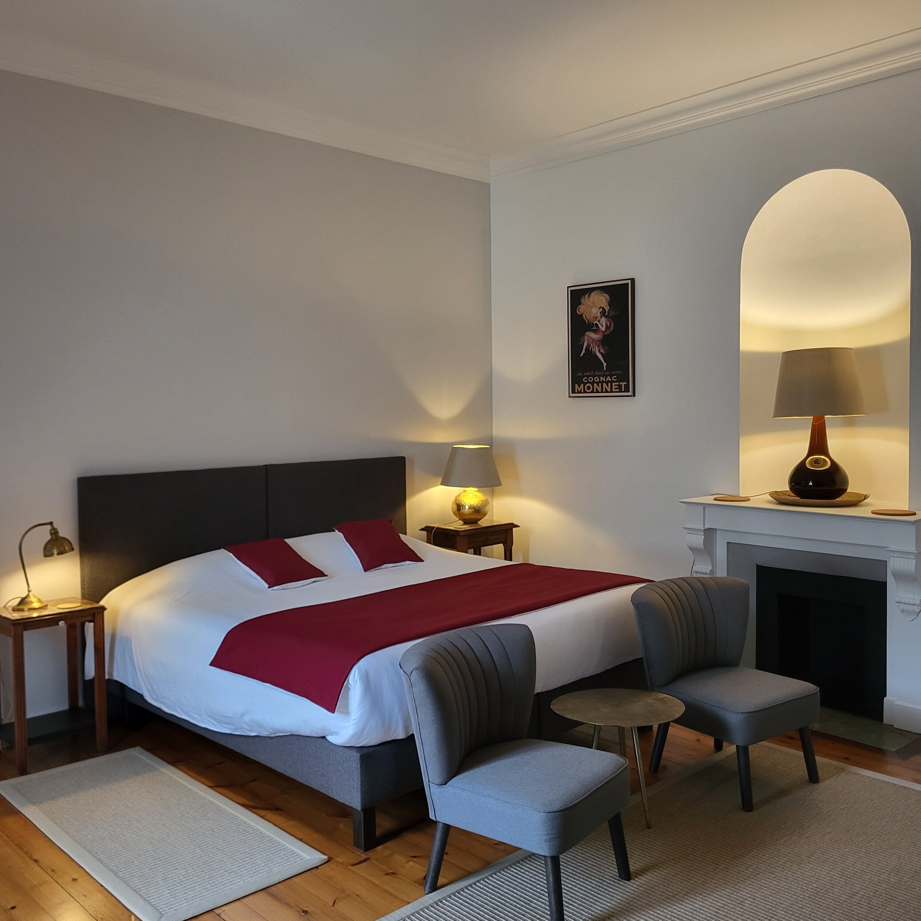 A hotel room with a large bed, two bedside tables with lamps, a fireplace, and a small armchair.