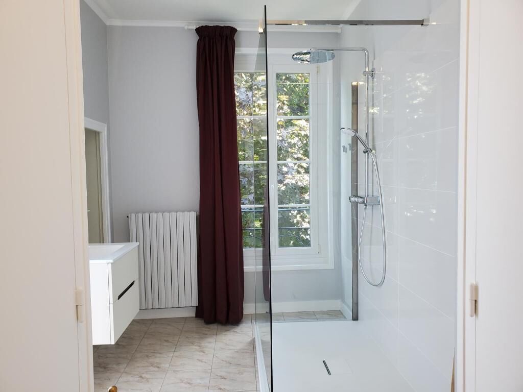 Een moderne badkamer met een douchecabine van glas, een witte radiator en uitzicht op groen buiten.