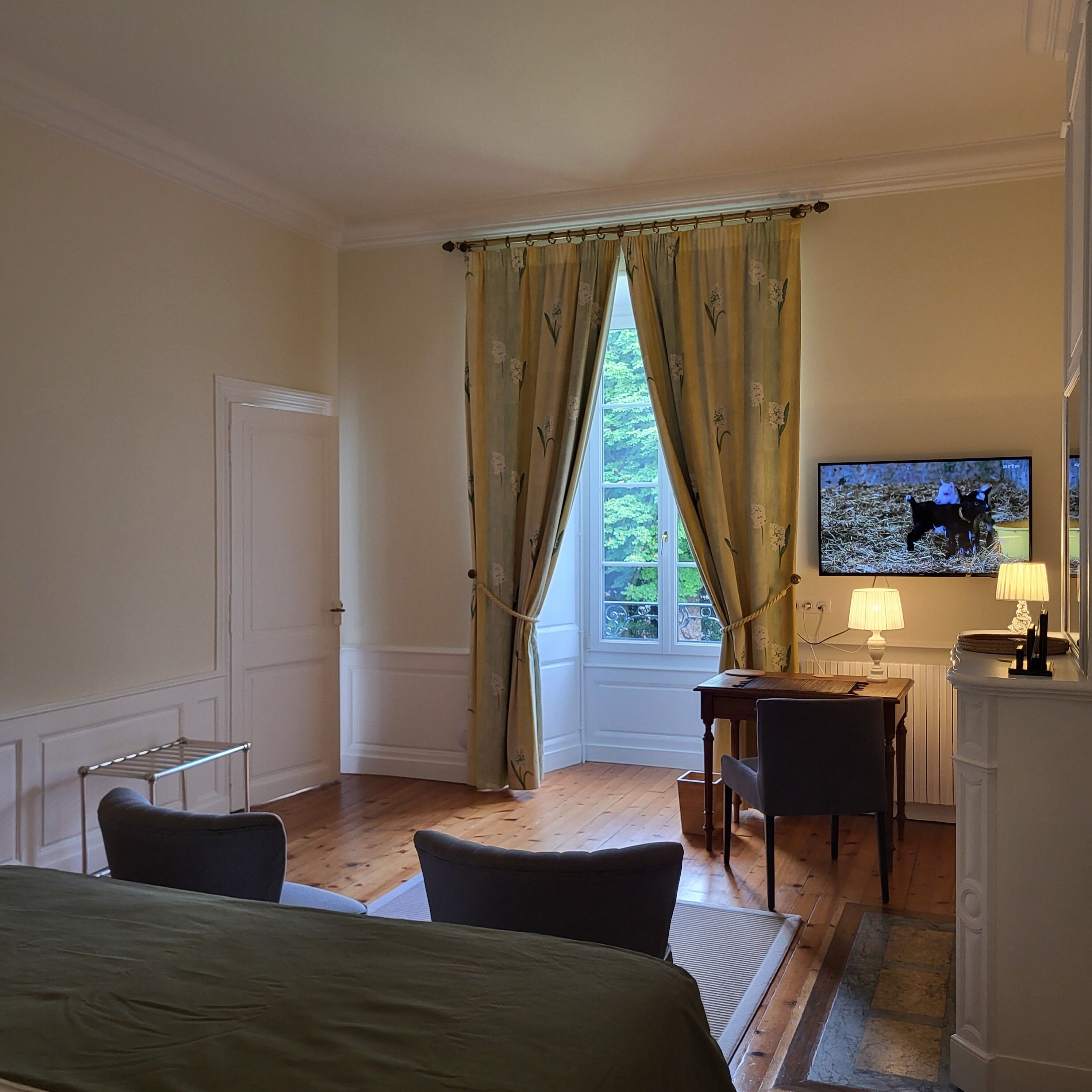 Une chambre d’hôtel comprenant un lit, un bureau avec une chaise, une télévision et une fenêtre avec des rideaux.