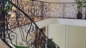 A staircase with ornate black metal railings, a framed picture on the wall, and potted plants. - Logis des Tourelles (Cognac)