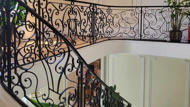Un escalier avec des rampes en métal noir ouvragé, un tableau encadré au mur et des plantes en pot.