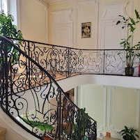 Uma escadaria com elegantes corrimãos de metal preto, um quadro na parede e plantas em vasos.