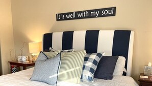 A neatly made bed with a striped headboard, a bedside table with a lamp, and a sign above the bed that reads "It is well with my soul". - Cozy apartment getaway in Holland (Holland)