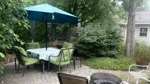 An outdoor patio with a table and chairs, a blue umbrella, and a fire pit. - Cozy apartment getaway in Holland (Holland)