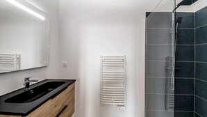 Een moderne badkamer met een zwart wastafel, houten wastafelmeubel, een spiegel, een handdoekhouder en een douchecabine van glas.