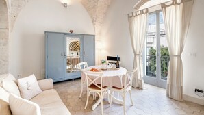 A room with a round table, white chairs, a blue cabinet, and a large window with curtains. - CA'milla Suite Home (Ostuni)