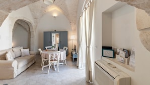 A cozy room with a stone archway, a dining area with a table and chairs, a sofa, and a built-in air conditioning unit. - CA'milla Suite Home (Ostuni)