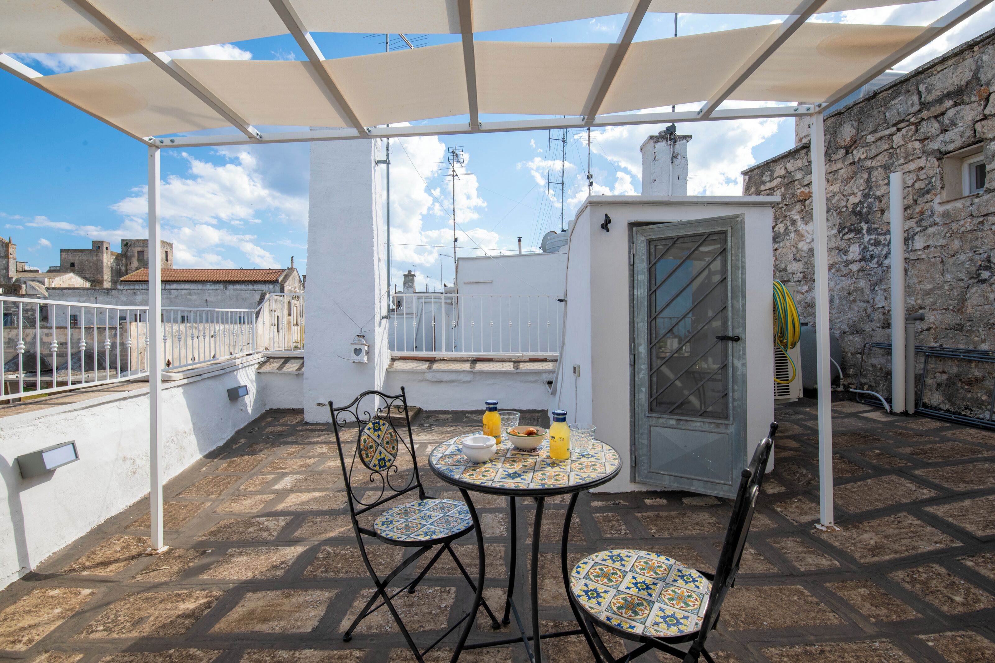 Un área de estar al aire libre con techo, una mesa, sillas, una puerta pequeña y vistas de la ciudad.