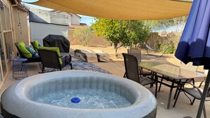 Un bain à remous avec une table et des chaises à proximité, le tout entouré d’une terrasse couverte.