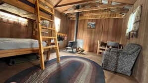 Et hyggeligt sommerhusinteriør med køjeseng, skrivebord, stol og pejs.
