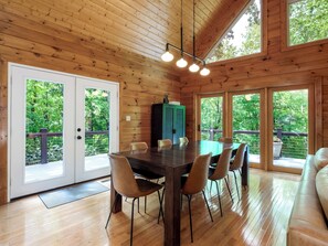 A wooden cabin with a dining area, large windows, and a view of the forest.