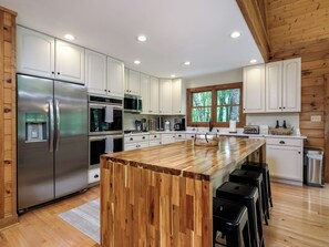 A modern kitchen with stainless steel appliances, a wooden island, and a large window.