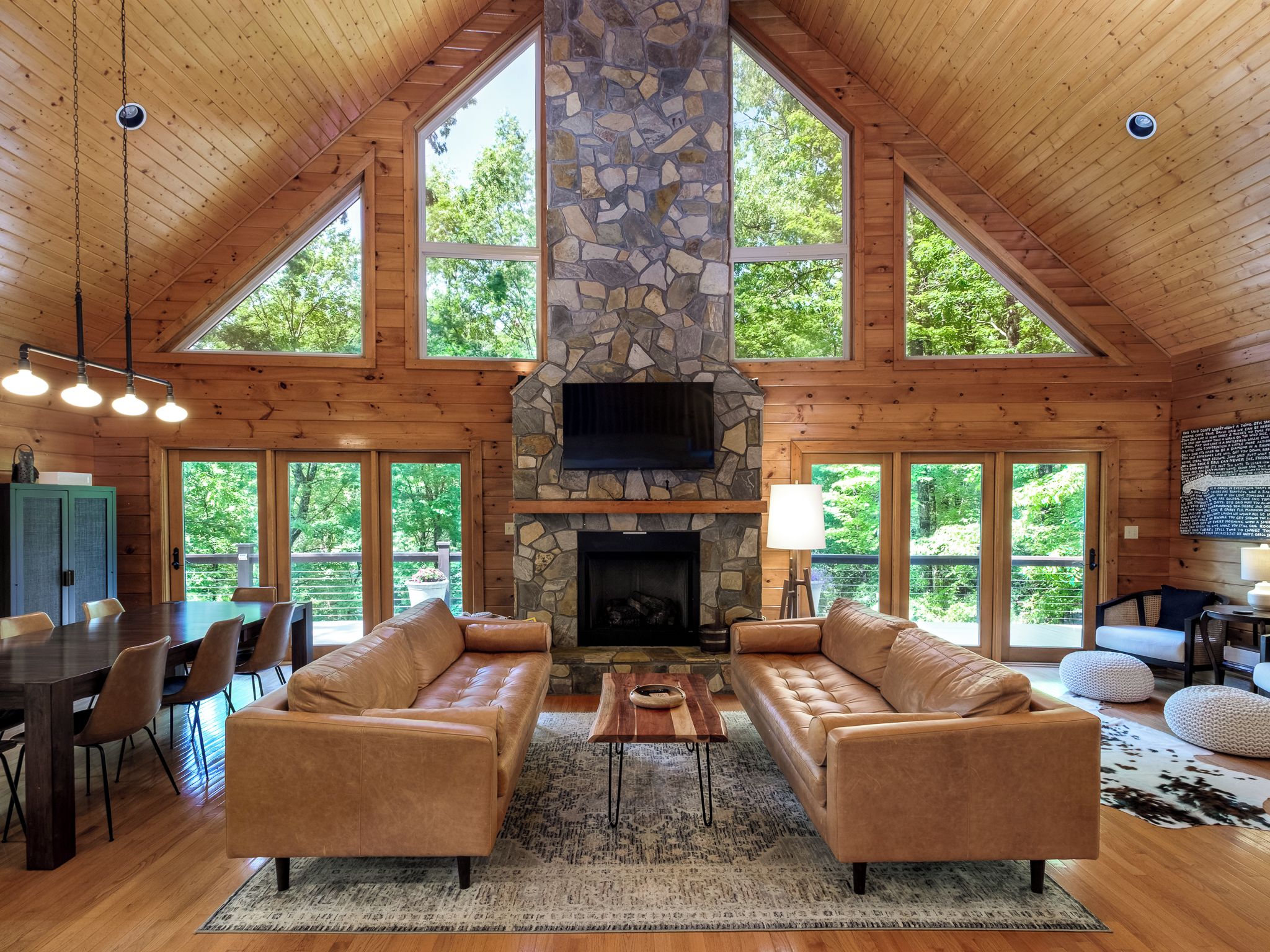 A spacious living room with a stone fireplace, leather sofas, and large windows offering a view of the outdoors.