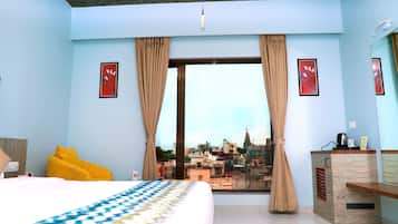 Habitación de hotel con cama, ventana con cortinas, vistas a la ciudad, escritorio con espejo y una pequeña mesa con hervidor.