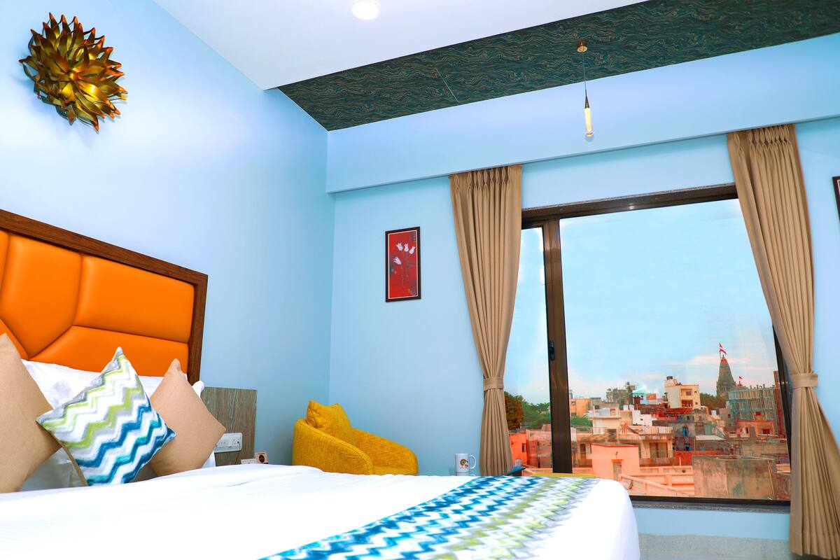 Quarto de hotel com uma janela grande, cama com colcha estampada e vista para a cidade.